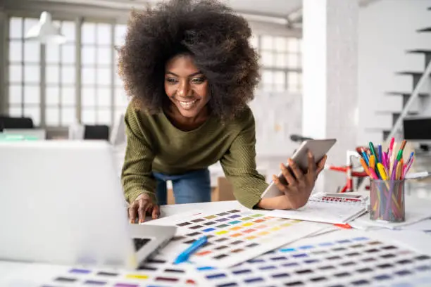 Fashion designer working in studio. Young black woman in an office smiling to camera, close up