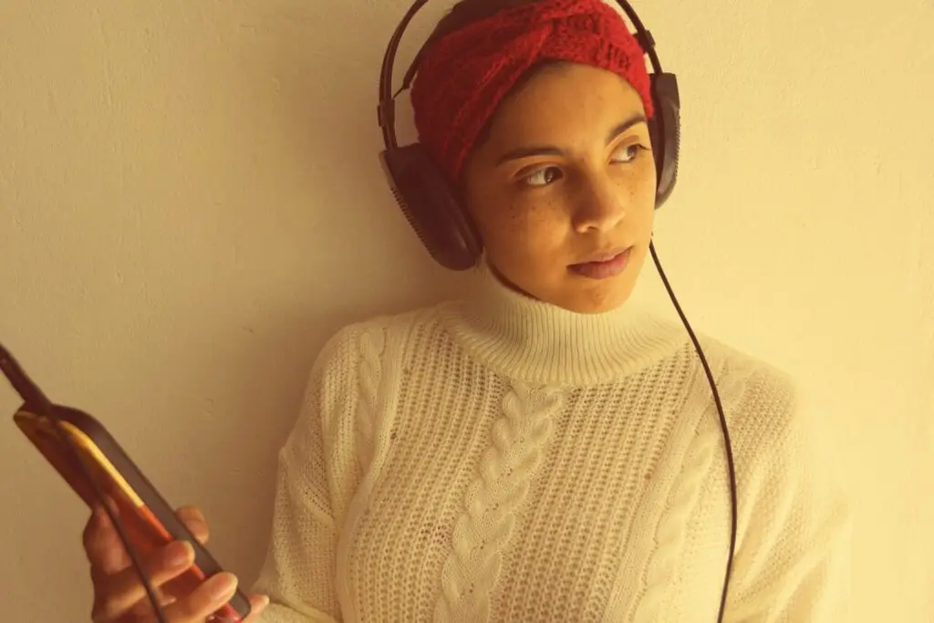 mulher de fone e celular, blusa de gola alta branca e turbante vermelho, uma mulher negra de pele clara.